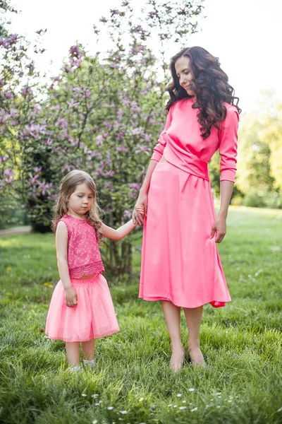 A young beautiful mother with a little daughter is walking along the spring park. Portrait of a mother and a little daughter near the blooming magnolia. Spring. A happy family. Heat. — Stock Photo, Image