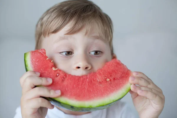 Un niño pequeño y lindo de 4 años está comiendo una sandía. Verano. Calor. Sandía. Retrato de un niño feliz con una sandía. Tonos brillantes . —  Fotos de Stock