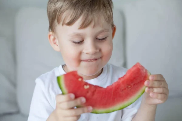 Un niño pequeño y lindo de 4 años está comiendo una sandía. Verano. Calor. Sandía. Retrato de un niño feliz con una sandía. Tonos brillantes . — Foto de Stock
