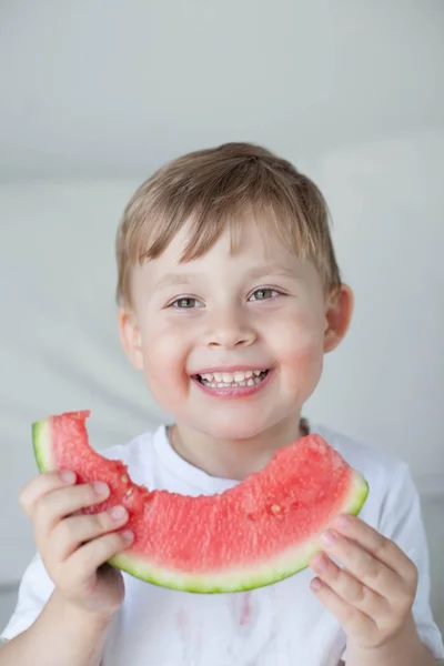 En liten söt pojke 4 år äter en vattenmelon. Sommaren. Värme. Vattenmelon. Porträtt av en glad pojke med en vattenmelon. Ljusa nyanser. — Stockfoto