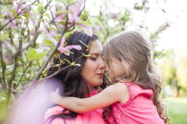 Küçük kızı olan genç güzel bir anne bahar park boyunca yürüyor. Bir anne ve çiçek açan magnolia yakınındaki küçük bir kız portresi. Bahar. Mutlu bir aile. Isı.