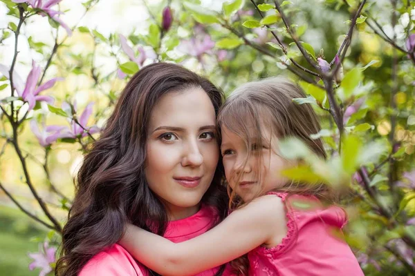 Una joven y hermosa madre con una hija pequeña está caminando por el parque de primavera. Retrato de una madre y una pequeña hija cerca de la floreciente magnolia. Primavera. Una familia feliz. Calor . —  Fotos de Stock