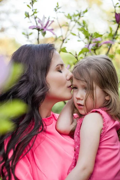 Egy fiatal gyönyörű anya a kislányom séta a tavaszi park. Portréja egy anya és egy kis lánya a virágzó magnólia közelében. Tavaszi. Egy boldog család. Hő. — Stock Fotó