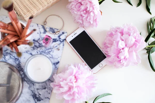 Peonies. Bouquet of pink peonies, candle, wicker bag, scarf, perfume, jewelry, phone on white table. Cosmetic table. Spring.