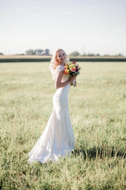 Güneş ışığı içinde güzel bir gelin portresi. Gelinlik genç mutlu kadın alanına yürüyor. Buket. Çiçekler. Yaz. Rahat.