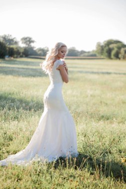 Güneş ışığı içinde güzel bir gelin portresi. Gelinlik genç mutlu kadın alanına yürüyor. Buket. Çiçekler. Yaz. Rahat.