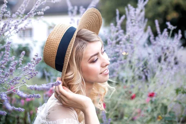 若いブロンドはフラワー ガーデンで歩いています 若い女性は 花と麦わら帽子に保持しています ラベンダー — ストック写真