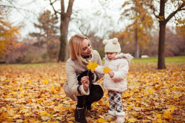 Genç anne ve küçük kızı sonbaharda yürümek. Anne ve kızı oynamak. Sıcak kış. Parlak sonbahar. Rahat.