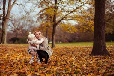 Genç anne ve küçük kızı sonbaharda yürümek. Anne ve kızı oynamak. Sıcak kış. Parlak sonbahar. Rahat.