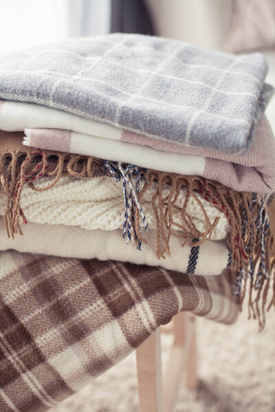Plaids. Autumn cozy interior. A stack of warm blankets lie on a wooden chair. Autumn. Winter.