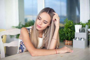 Genç güzel sarışın mavi gözlü bir kafede oturuyor. Mutlu bir kadın portresi. Moda. Makyaj. Yaz.