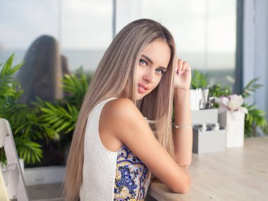 Genç güzel sarışın mavi gözlü bir kafede oturuyor. Genç bir kadın bir kapuçino kupa onun elinde tutar. Mutlu bir kadın portresi. Moda. Makyaj. Yaz.