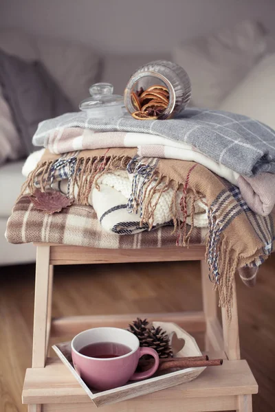 チェック模様 熱いお茶のカップ 秋の居心地の良いインテリア 木製の椅子は暖かい毛布のスタックです キャンドル 円錐形 バスケット シナモン 本とメガネ — ストック写真