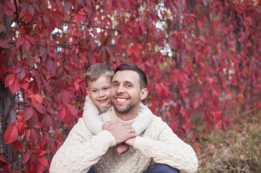 Baba ve küçük oğlu sonbahar parkta yürümek. Parlak, sıcak sonbahar. Kırmızı yaprakları. Rahat. Baba ve oğlu örme kazak portre.