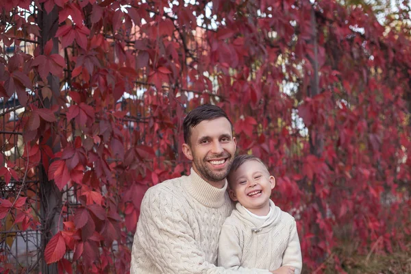 お父さんと息子の小さな秋の公園の中を歩きます。明るく、暖かい秋。赤の葉。居心地の良い。お父さんと息子のニット セーターでの肖像画. — ストック写真