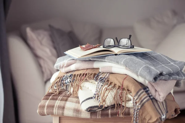 Плайды. Осенний уютный интерьер. На деревянном стуле - стопка теплых одеял. Книга и очки. Осень. Зима . — стоковое фото
