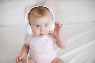 Yatağın üstüne oturan kulaklıklar ile küçük küçük mavi gözlü kız pembe elbiseli. Kız müzik kulaklık ile oynuyor. Rahat. Ana sayfa.