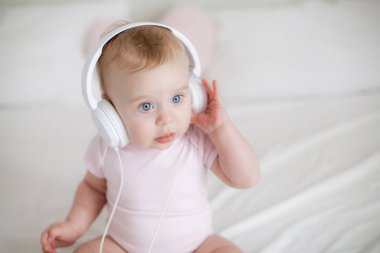 Yatağın üstüne oturan kulaklıklar ile küçük küçük mavi gözlü kız pembe elbiseli. Kız müzik kulaklık ile oynuyor. Rahat. Ana sayfa.