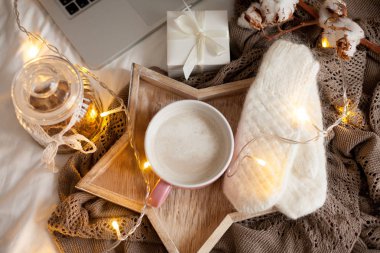 Bir fincan sıcak cappuccino bir ahşap tepsi yatağım. Rahat dekor. Kahvaltı. Kupa, ekose, pamuk, dizüstü bilgisayar, mum. Hediye kutusu ve örme eldivenler. Noel ışıkları. Tatil.