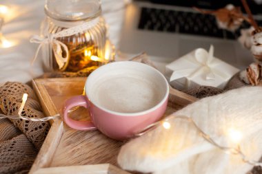 Bir fincan sıcak cappuccino bir ahşap tepsi yatağım. Rahat dekor. Kahvaltı. Kupa, ekose, pamuk, dizüstü bilgisayar, mum. Hediye kutusu ve örme eldivenler. Noel ışıkları. Tatil.