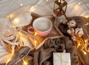 Bir fincan sıcak cappuccino bir ahşap tepsi yatağım. Rahat dekor. Kahvaltı. Kupa, ekose, pamuk, mum. Hediye kutusu ve örme eldivenler. Noel ışıkları. Tatil.