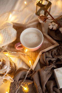 Bir fincan sıcak cappuccino bir ahşap tepsi yatağım. Rahat dekor. Kahvaltı. Kupa, ekose, pamuk, mum. Hediye kutusu ve örme eldivenler. Noel ışıkları. Tatil.