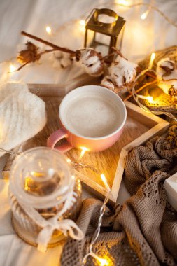 Bir fincan sıcak cappuccino bir ahşap tepsi yatağım. Rahat dekor. Kahvaltı. Kupa, ekose, pamuk, mum. Hediye kutusu ve örme eldivenler. Noel ışıkları. Tatil.