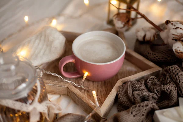 木製トレイに熱いカプチーノのマグカップはベッドの上です 居心地の良い内装 マグカップ チェック柄 キャンドル ギフト用の箱 ニットのミトン クリスマスの照明 — ストック写真