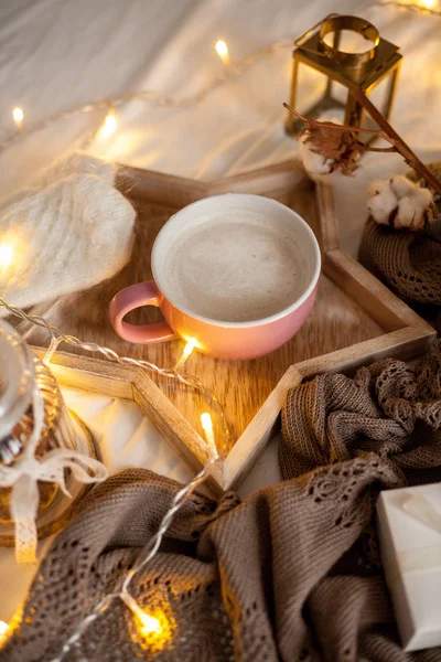 Bir fincan sıcak cappuccino bir ahşap tepsi yatağım. Rahat dekor. Kahvaltı. Kupa, ekose, pamuk, mum. Hediye kutusu ve örme eldivenler. Noel ışıkları. Tatil.