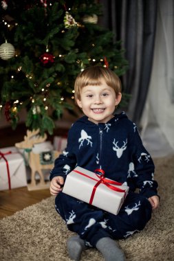 Noel ağacının yanında oturan ve bir kutu bir hediye ile tutan küçük şirin çocuk. Tatil. Noel. Yeni yıl. Bir çocuk 3 yıllık Noel pijama.