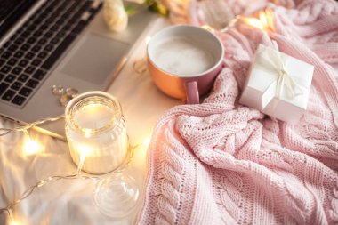 Rahat dekor. Bir fincan kapuçino. Bir cam kavanozun içinde mum, pembe örgü battaniye, gül, laptop. Rahat. Sonbahar.
