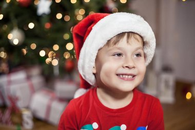 Noel ağacı yakınındaki bir Noel Baba şapkalı bir mutlu 4 yaşındaki çocuk portresi. Noel. Tatil. Yeni yıl. Mutluluk. Çocuk. Rahat.