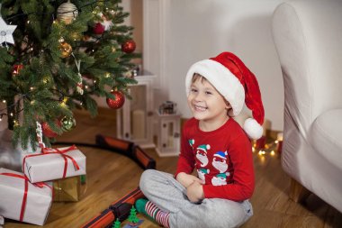 Noel ağacı yakınındaki bir Noel Baba şapkalı bir mutlu 4 yaşındaki çocuk portresi. Noel. Tatil. Yeni yıl. Mutluluk. Çocuk. Rahat.