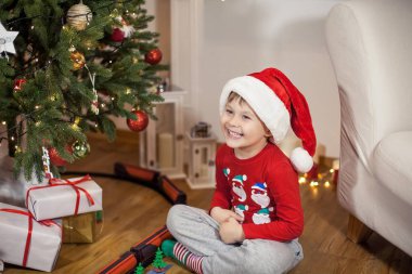 Noel ağacı yakınındaki bir Noel Baba şapkalı bir mutlu 4 yaşındaki çocuk portresi. Noel. Tatil. Yeni yıl. Mutluluk. Çocuk. Rahat.