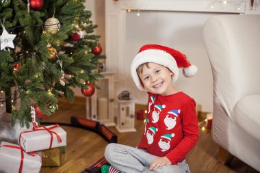 Noel ağacı yakınındaki bir Noel Baba şapkalı bir mutlu 4 yaşındaki çocuk portresi. Noel. Tatil. Yeni yıl. Mutluluk. Çocuk. Rahat.