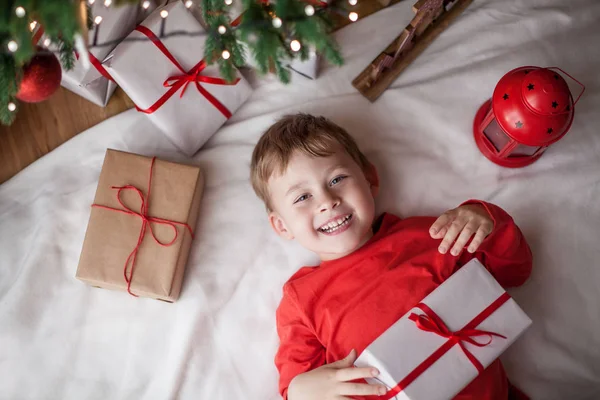 Küçük mutlu sevimli çocuk Noel ağacının yanında yatıyor ve bir hediye kutusu tutar. Çocuk. Noel ruh. Tatil. Noel. Yeni yıl.