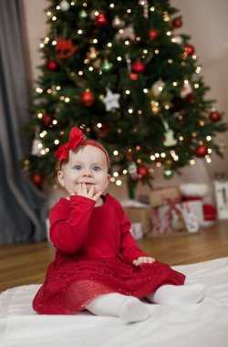 Noel ağacının yanında oturan kırmızı elbiseli mavi gözlü küçük kız. Mutlu bebek. Noel homeliness. Tatil.