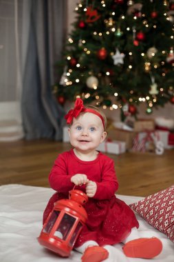 Noel ağacının yanında oturan kırmızı elbiseli mavi gözlü küçük kız. Mutlu bebek. Noel homeliness. Tatil.