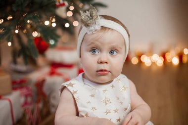 Noel ağacı yanında küçük bebek. Şirin mavi gözlü bebek başında bir taç ile bir altın elbiseli. Mutluluk. Tatil. Noel. Yeni yıl. Rahat.
