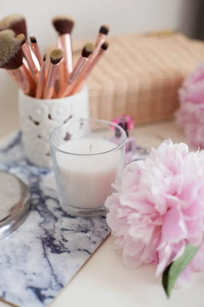 Peonies. Bouquet of pink peonies, candle, wicker bag, scarf, perfume, jewelry, phone on white table Cosmetic table