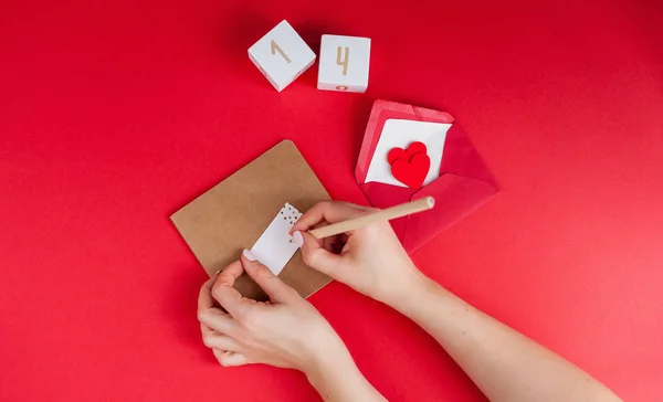 女性の手にはサインカード赤い背景の上 バレンタインデーのコンセプトです バレンタイン 番号を持つ木製キューブの心 — ストック写真
