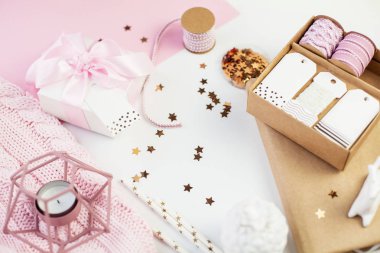Bahar dekor. Pembe bir kurdele, pırıltılar, kurdeleler, bir mum, bir defter pembe ve beyaz arka plan üzerinde beyaz hediye kutusu. Anneler günü.