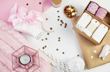 Bahar dekor. Pembe bir kurdele, pırıltılar, kurdeleler, bir mum, bir defter pembe ve beyaz arka plan üzerinde beyaz hediye kutusu. Anneler günü.