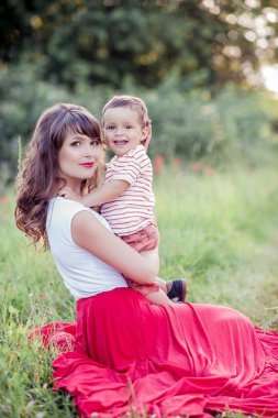 Güzel bir aile haşhaş alanına yürüyor. Küçük oğlu olan genç bir anne yürüyor. Yaz. Bahar.