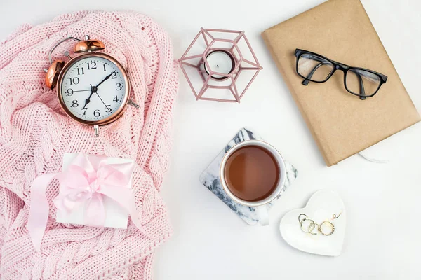 Spring decor. Womens clothing. Alarm clock, gift box with a pink ribbon, jewelry, a candle, a mug of tea, glasses, a notebook on a white background.