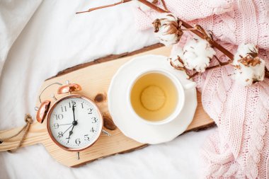 Çalar saat, yatak, pembe örgü battaniye çay ile güzel bir beyaz fincan. Yatakta kahvaltı. Sabah. Bahar.