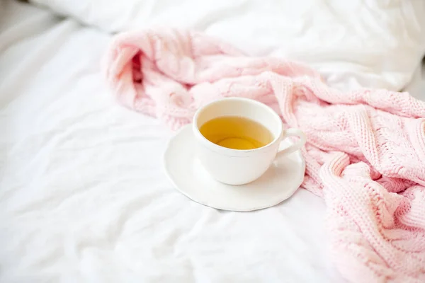 Beautiful white cup with tea on the bed, pink knitted plaid. Breakfast in bed. Morning. Spring.