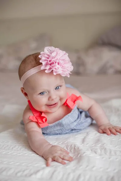 Sevimli küçük mavi gözlü kız başında çiçekli bir elbise. Bebek yatakta yatıyor. 4 aylık bir çocuk portresi — Stok fotoğraf