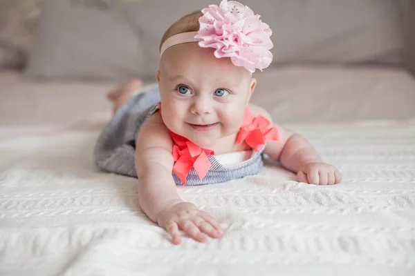 Sevimli küçük mavi gözlü kız başında çiçekli bir elbise. Bebek yatakta yatıyor. 4 aylık bir çocuk portresi — Stok fotoğraf