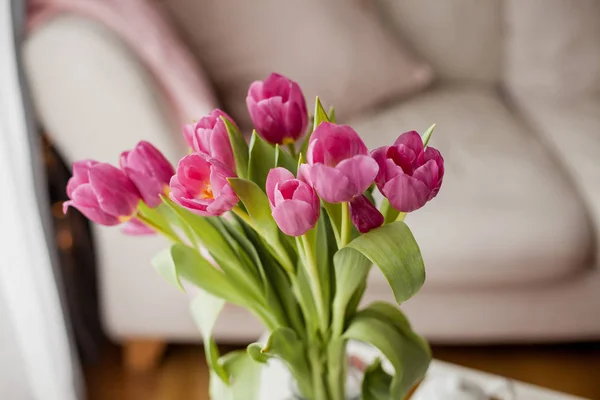 Frühjahrsinnenraum. Ein Strauß Tulpen in einer Glasvase, ein goldenes Tablett, eine Tasse, eine Teekanne, ein rosa Plaid, ein Sofa. gemütlich. — Stockfoto